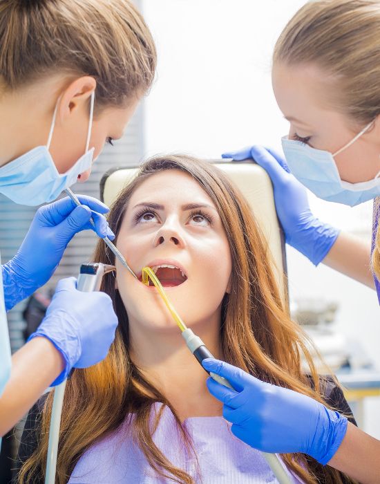 Patient receiving dental treatment from two dental professionals, showcasing advanced restorative dentistry techniques at NuSmile Implant Studio.